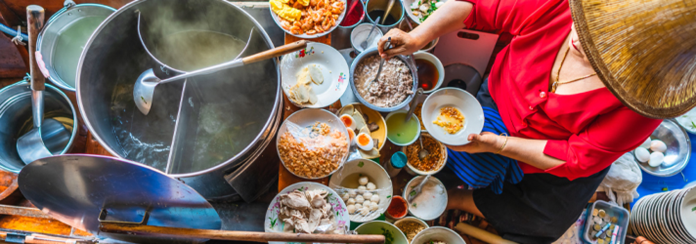 A local Vietnamese lady is stirring a pot of food, surrounded by multiple bowls of local ingredients.
