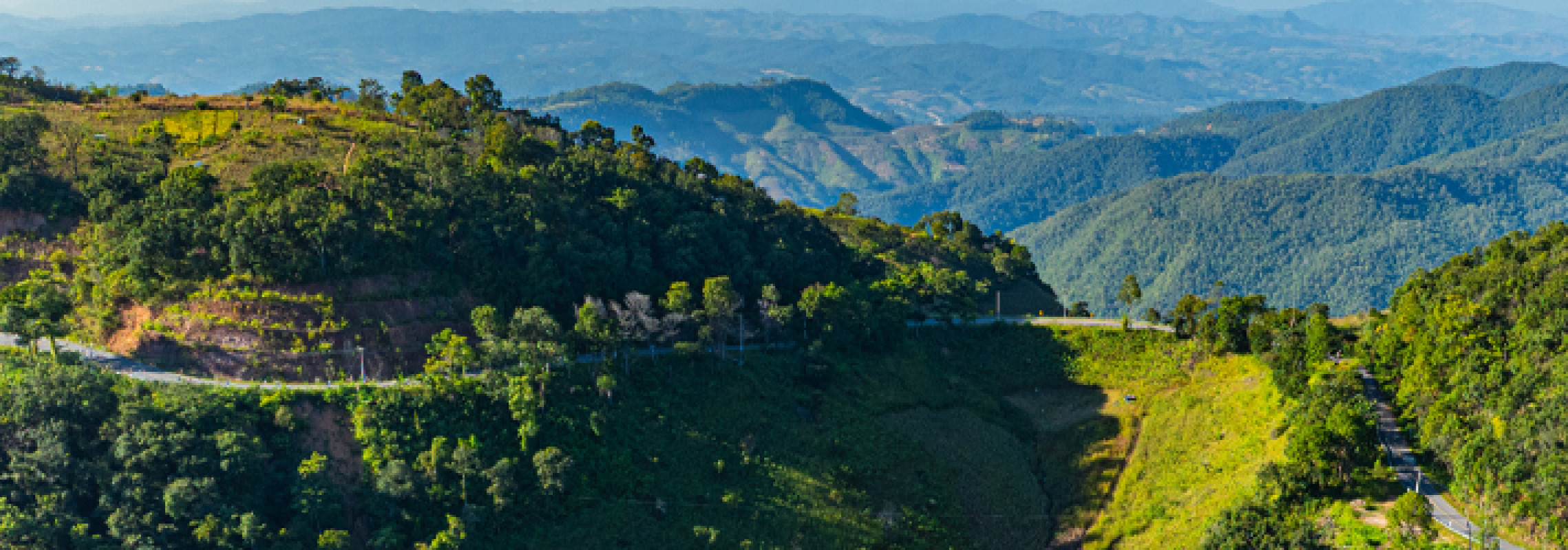 A mountainous landscape in South East Asia with a road running through it.